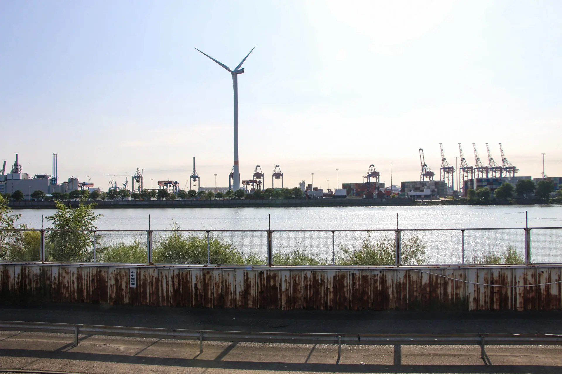 Windrad und Hafenkräne am Ufer